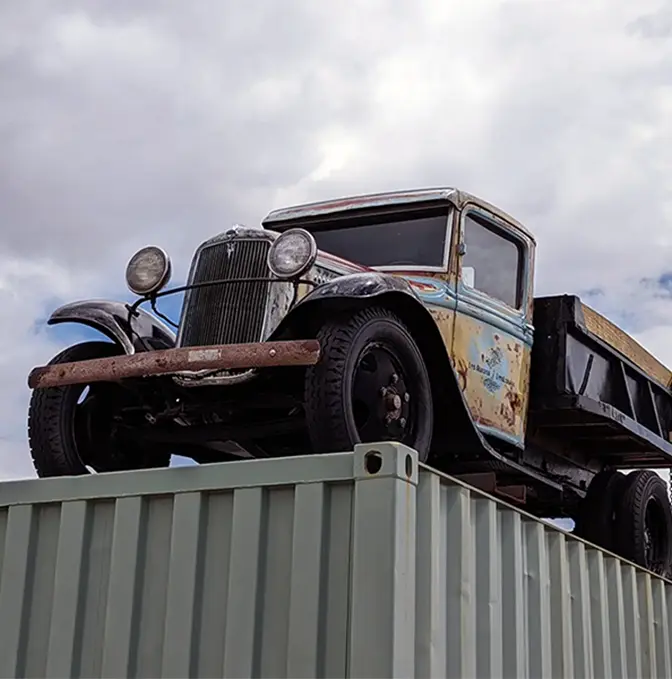 Vintage Los Alamos Landscaping truck displayed on top of a shipping container under a cloudy sky.