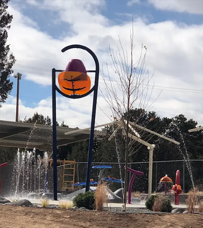 A young child standing under a cascading water feature at the splash pad.